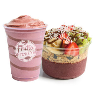 A pairing of a thick, pink smoothie with chocolate swirl in a branded Frutta Bowls cup and an acai bowl topped with banana slices, strawberries, kiwi, shredded coconut, and a drizzle of nut butter, all layered over granola and a deep berry smoothie base.