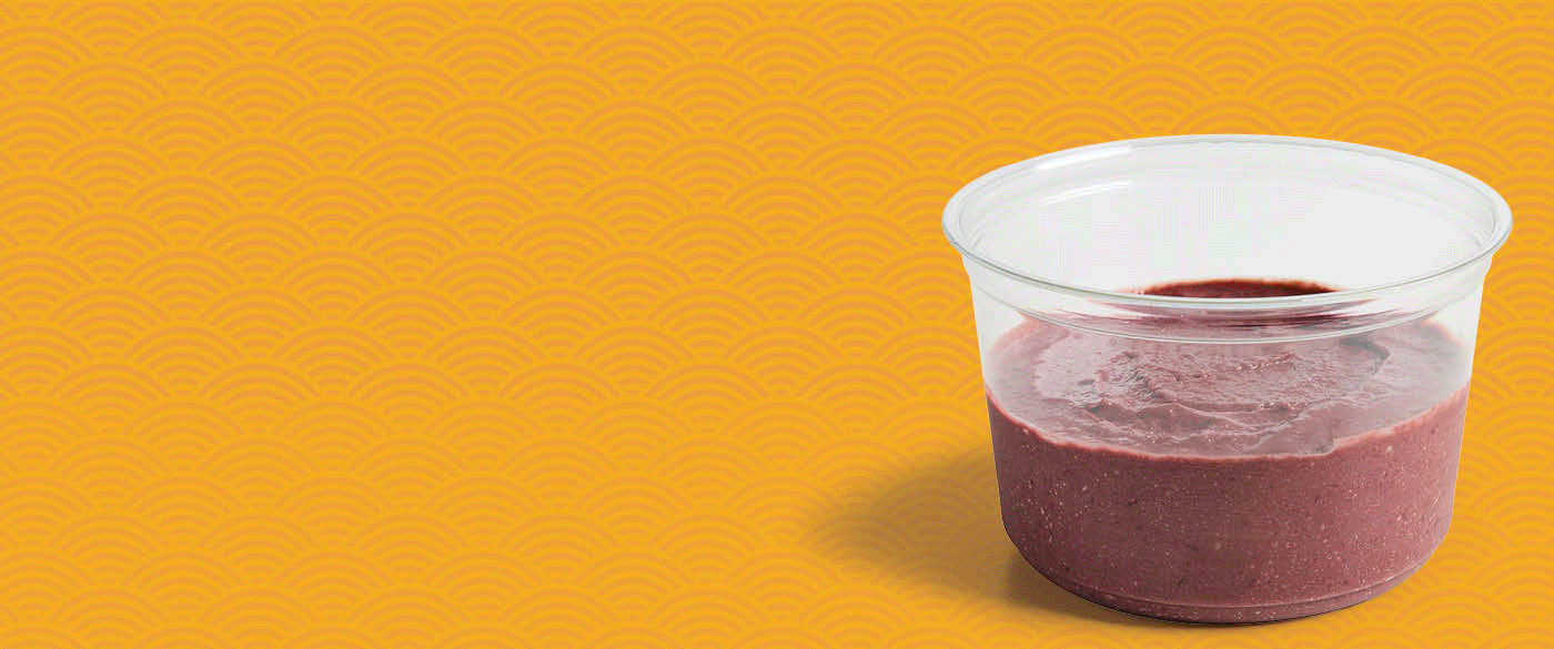 Clear plastic bowl filled with a thick, blended açaí base against a yellow patterned background.