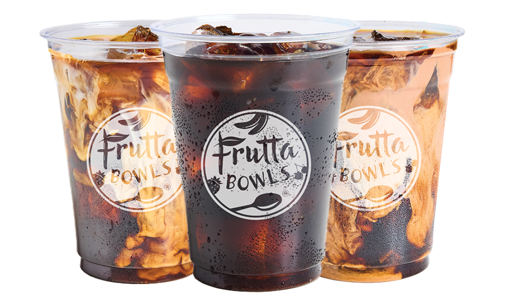 Three clear plastic cups of iced drinks with Frutta Bowls logos, featuring a dark center drink and two cream-swirled drinks behind it on a light gray background.
